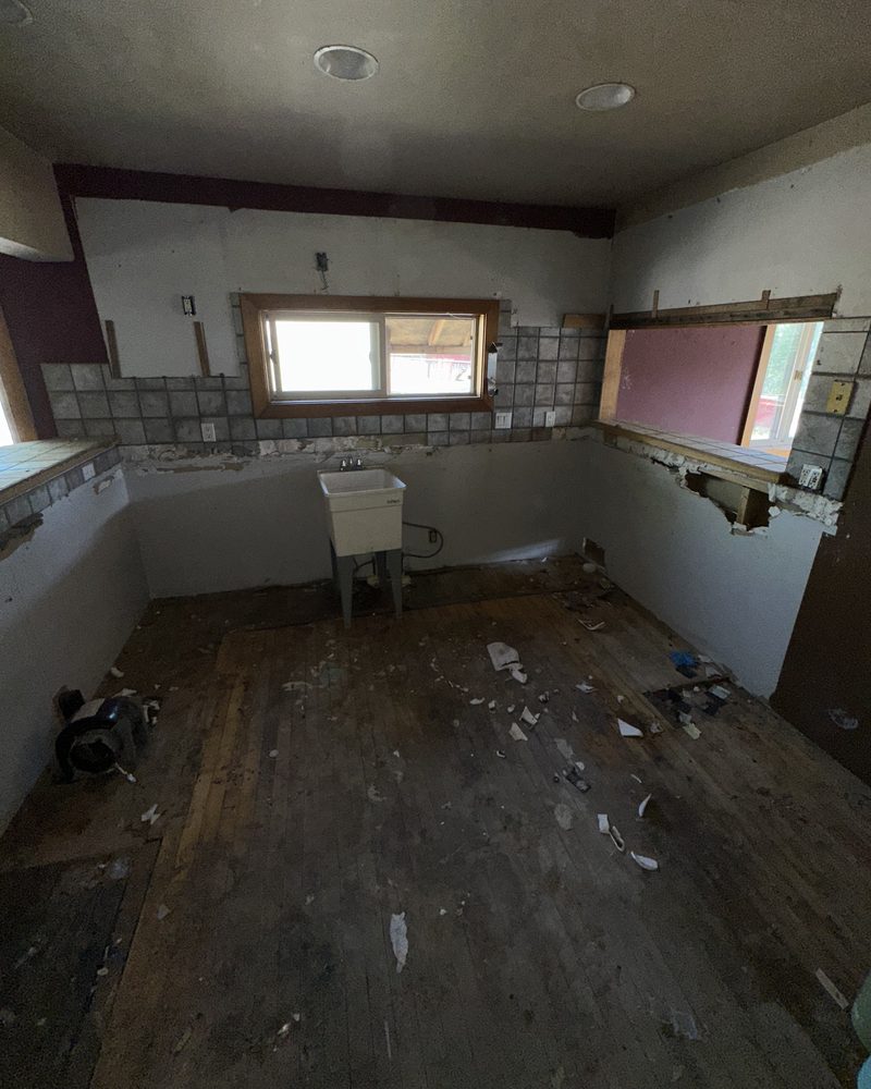 The same house: the kitchen, before: gutted, with a laundry sink and a torn-up floor